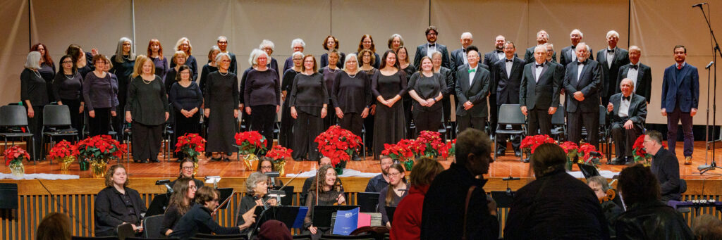 Full chorus and orchestra on stage surrounded by poinsettias
