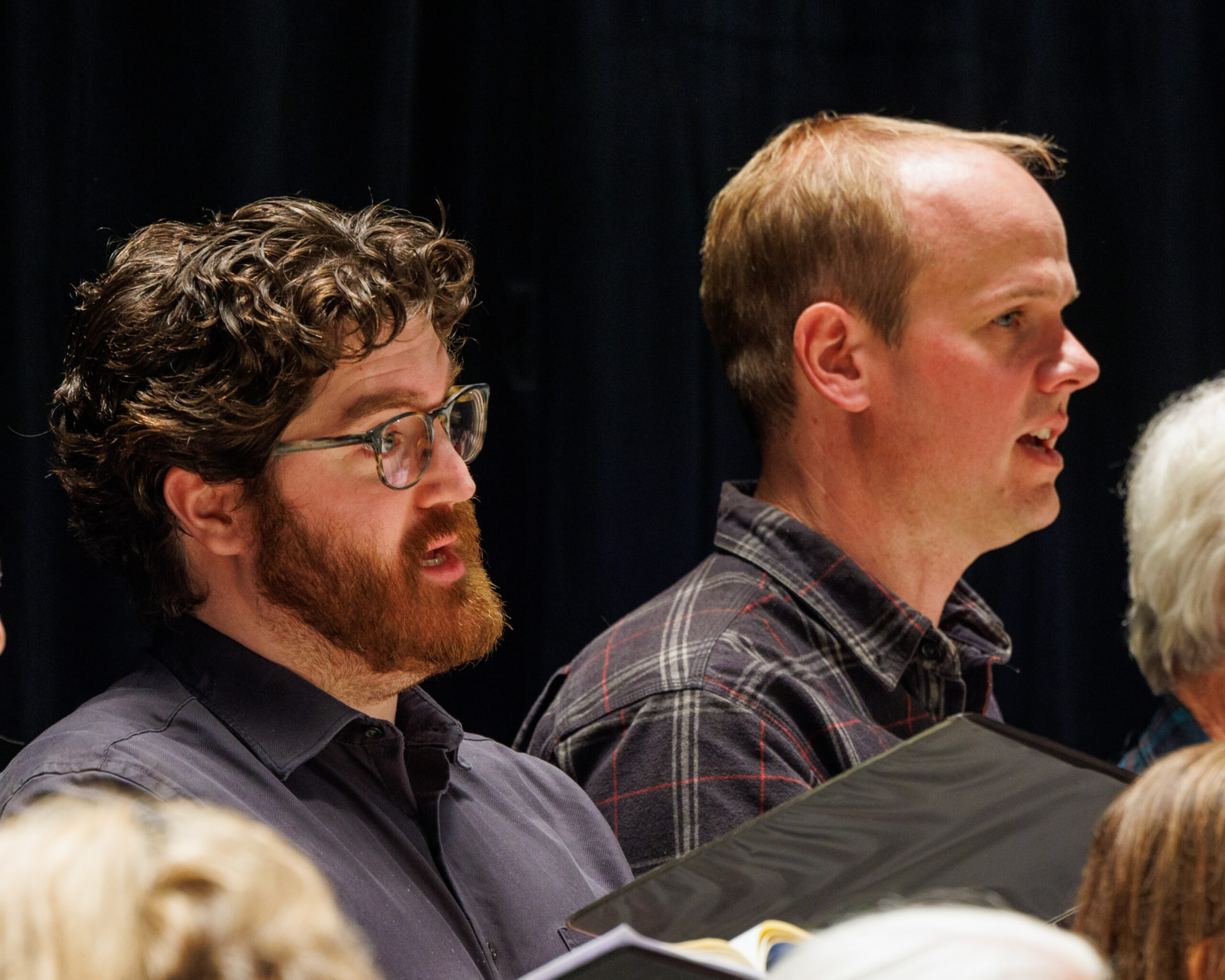 Two singers reading from their folders during rehearsal